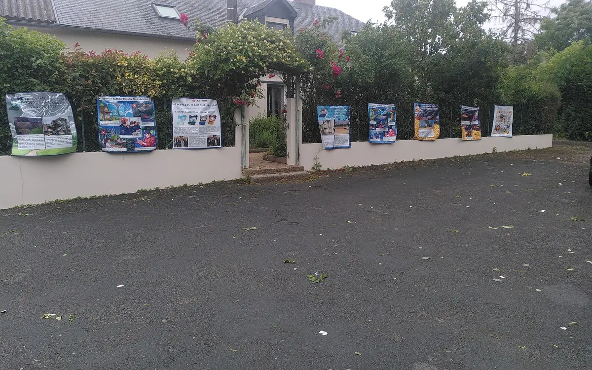 Des panneaux de l'exposition « La Mayenne, territoire résilient » accrochés le long du muret et de la haie, devant la ferme de Bel-Air.